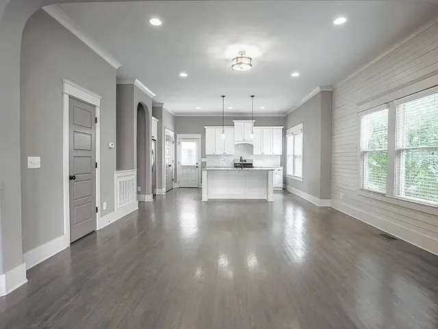 a view of a kitchen and an empty room with wooden floor and a window