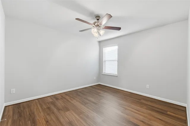 a view of an empty room with wooden floor and a ceiling fan