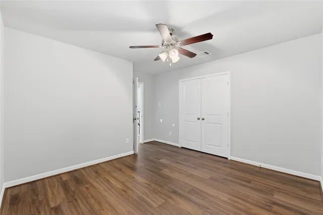 an empty room with wooden floor closet and windows