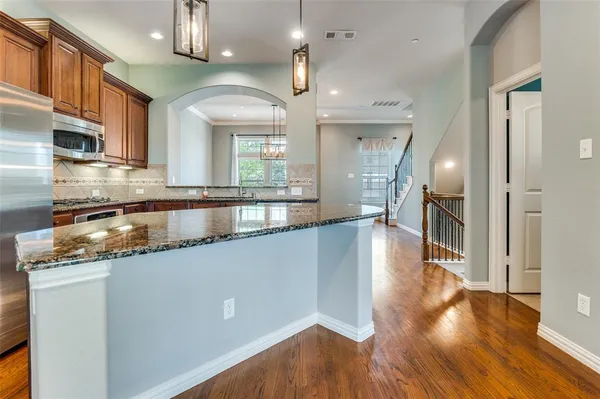 a kitchen with kitchen island granite countertop wooden floors and a view of living room