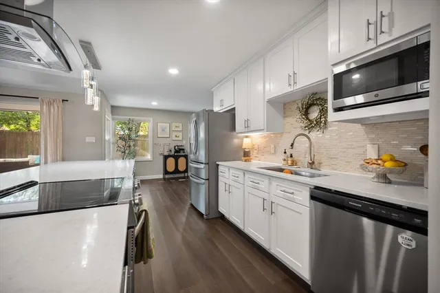 a kitchen with stainless steel appliances a stove a sink a oven a dining table and chairs with wooden floor