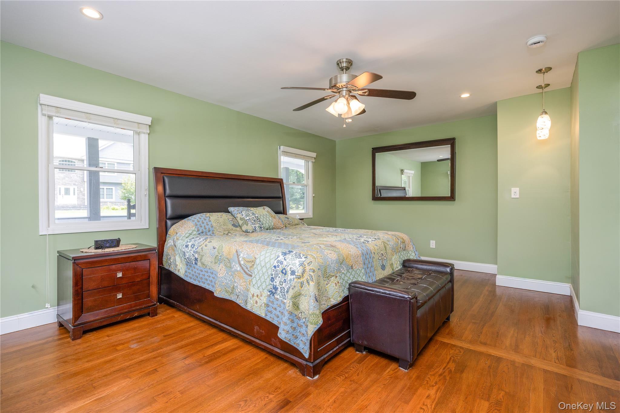 395 Ehrhardt Road Pearl River, NY 10965 - Photo 13 of 34 Spacious primary bedroom showcasing soft green walls, hardwood flooring, ceiling fan with integrated lighting, and a framed mirror