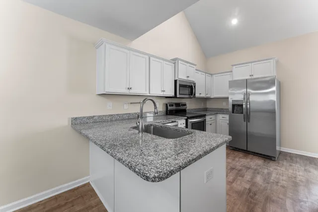 a kitchen with kitchen island granite countertop a sink dishwasher a refrigerator and white cabinets