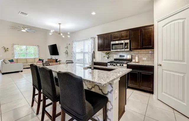 a kitchen with stainless steel appliances granite countertop a stove a refrigerator a sink a dining table and chairs