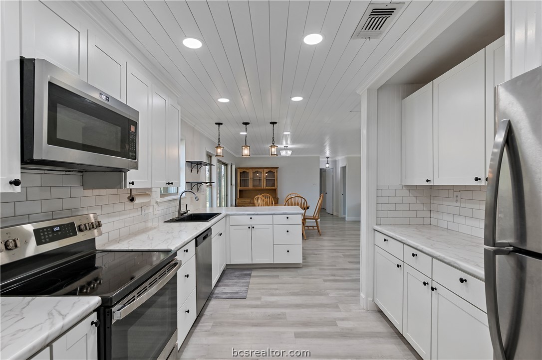8801 Old Reliance Road Bryan, TX 77808 - Photo 14 of 24 Bright kitchen with white cabinetry, subway tile backsplash, and stainless steel appliances.