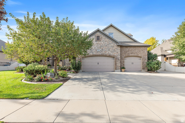 Stone and brick exterior with two integrated garages, a concrete driveway, and a landscaped front yard featuring mature trees