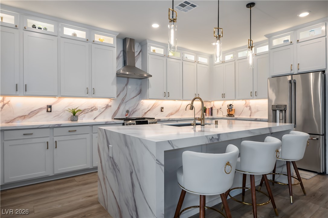 3018 Bounding Home Road North Las Vegas, NV 89086 - Photo 17 of 43 Kitchen with appliances with stainless steel finishes, wall chimney range hood, a kitchen island with sink, white cabinets, and backsplash