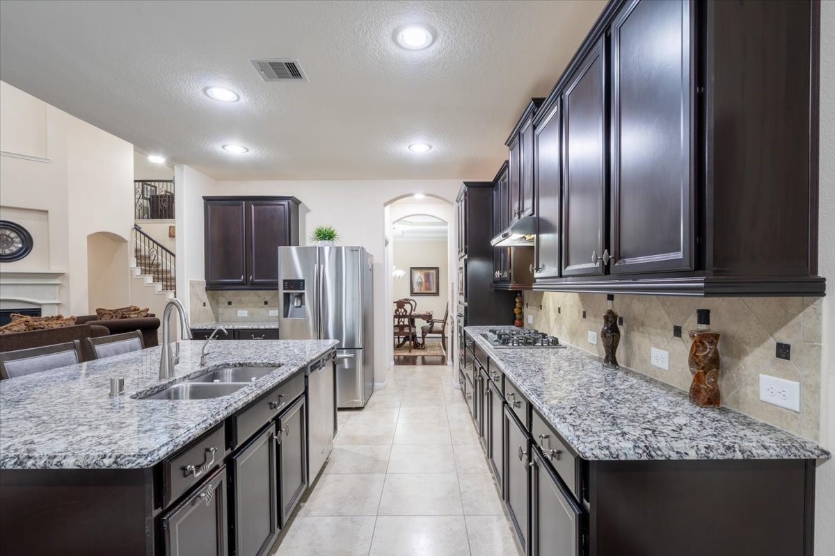 This kitchen features elegant dark wood cabinetry, granite countertops, and stainless steel appliances. It has a spacious layout with a central island and modern lighting, opening into a bright dining area.