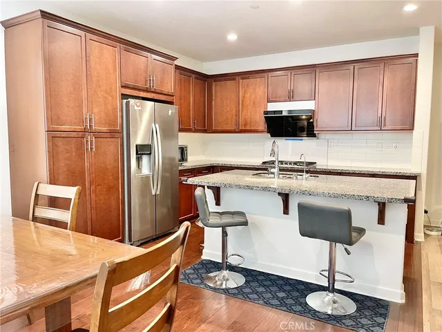 a kitchen with stainless steel appliances granite countertop a refrigerator a stove a sink cabinets and a dining table