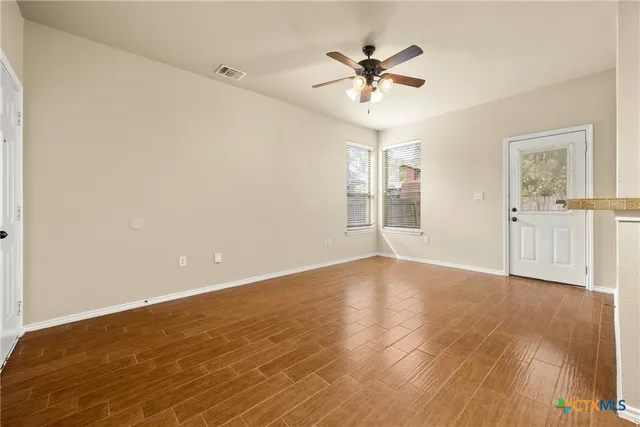 a view of an empty room with chandelier fan and wooden floor