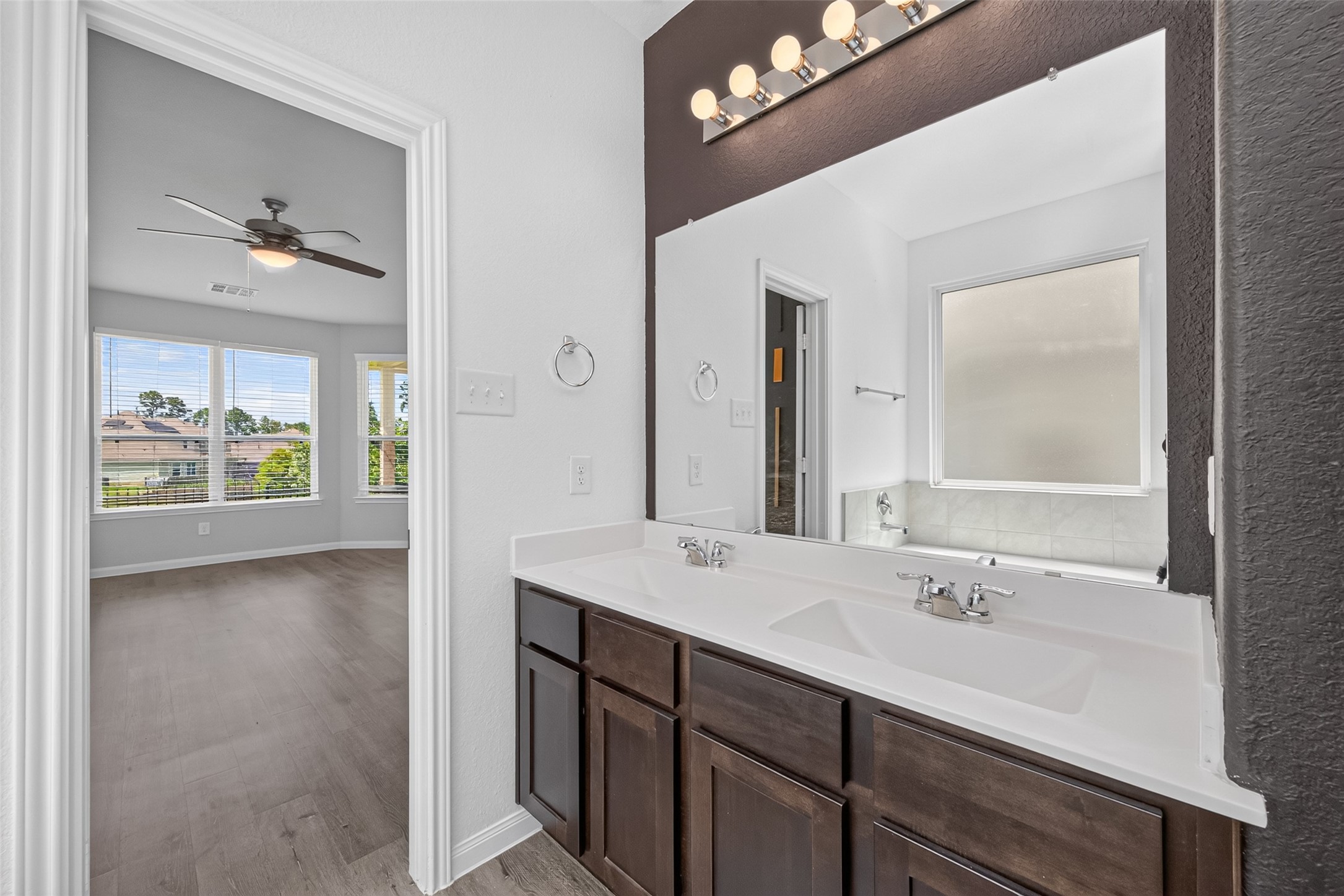 2526 Sturgeon Way Conroe, TX 77384 - Photo 24 of 49 This photo showcases a bright bathroom with a dual-sink vanity, modern fixtures, and a large mirror. Adjacent is a spacious bedroom featuring large windows with plenty of natural light and a ceiling fan, offering a comfortable living space.