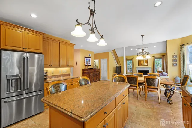 a view of a kitchen with kitchen island granite countertop a refrigerator a stove top oven a sink a dining table and chairs with wooden floor