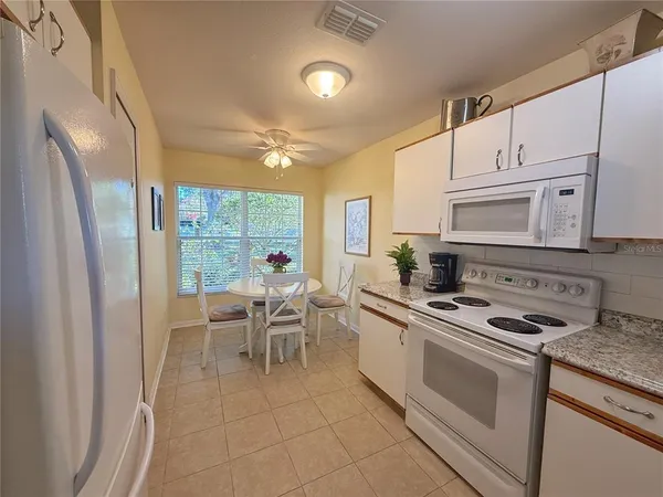 a kitchen with stainless steel appliances granite countertop a refrigerator a stove a sink a dining table and chairs with wooden floor