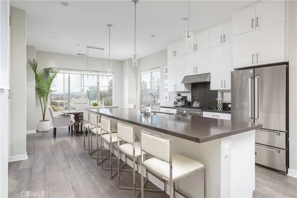 a kitchen with stainless steel appliances granite countertop a stove a refrigerator a kitchen island a dining table and chairs with wooden floor