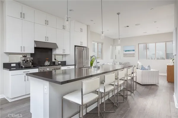 a kitchen with stainless steel appliances granite countertop a stove a sink a refrigerator and white cabinets with wooden floor