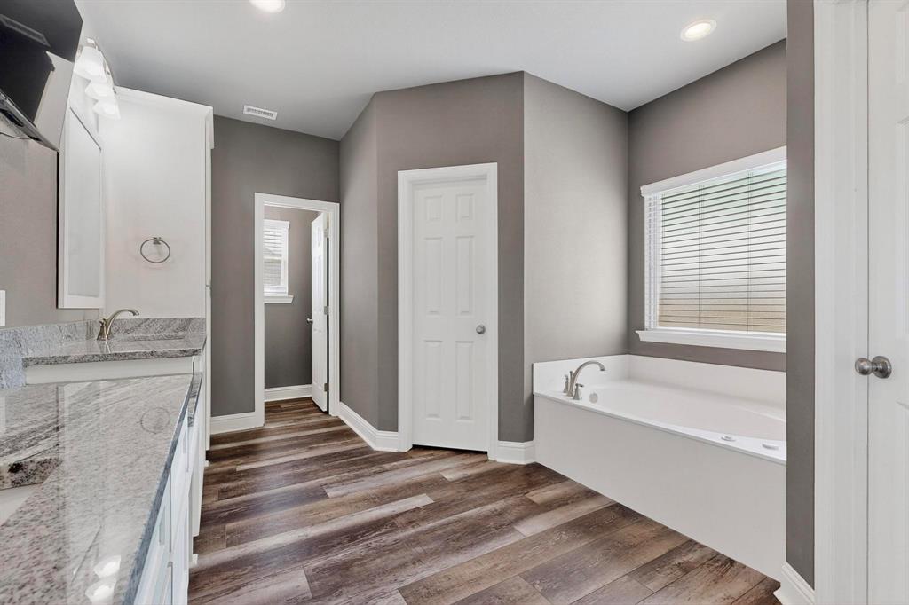 634 Gant Road Sherman, TX 75090 - Photo 22 of 40 Spacious bathroom featuring a built-in soaking tub with deck-mounted fixtures, double vanity with granite countertop, wood-finish flooring, and recessed lighting