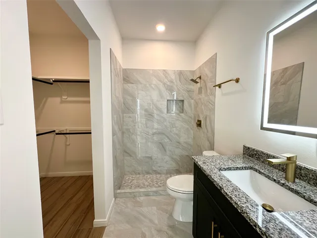 a bathroom with a granite countertop bathtub shower sink vanity mirror and toilet