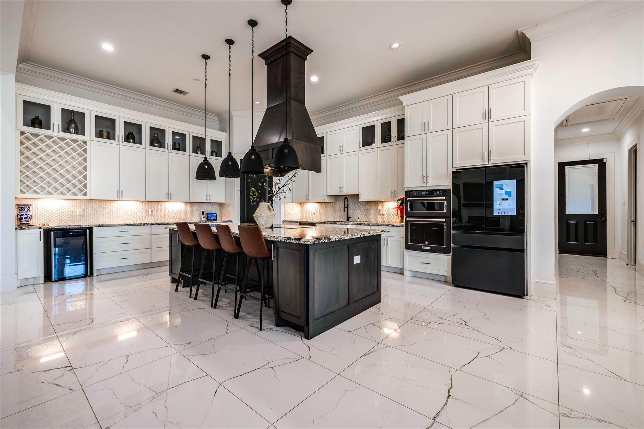4821 Walters Road Richmond, TX 77469 - Photo 23 of 50 his designer gourmet kitchen makes a bold statement with soaring custom cabinetry, dramatic ceiling-height finishes, and an oversized waterfall island perfect for entertaining. Featuring premium stainless steel appliances, elegant pendant lighting, marble-style flooring, and rich contrasting accents, the space blends timeless sophistication with modern functionality. The open-concept layout, expansive prep areas, built-in wine storage, and abundant natural light create a luxurious culinary experience