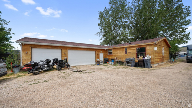 490 South Main Street Kamas, UT 84036 - Photo 17 of 25 Wood-sided structure featuring a two-car garage with white doors, a brown shingle roof, and exterior lighting fixtures