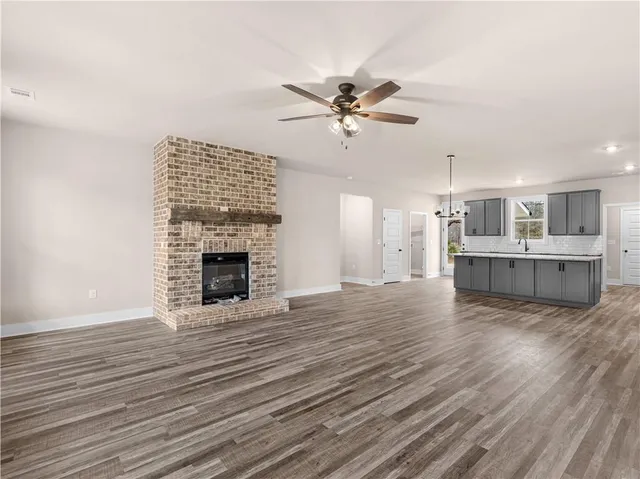 a view of a livingroom with a fireplace a ceiling fan and wooden floor