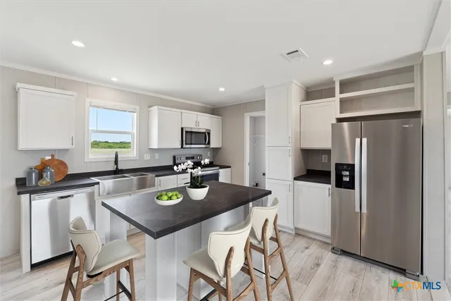 a kitchen with stainless steel appliances granite countertop a refrigerator a stove a sink a dining table and chairs with wooden floor