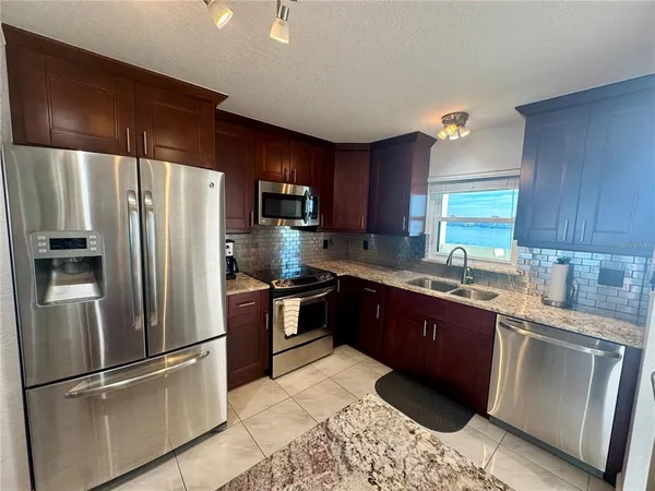 a kitchen with stainless steel appliances granite countertop a refrigerator a sink a stove a washer dryer and a refrigerator