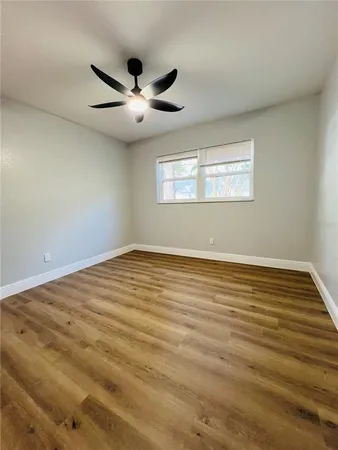 an empty room with wooden floor fan and windows