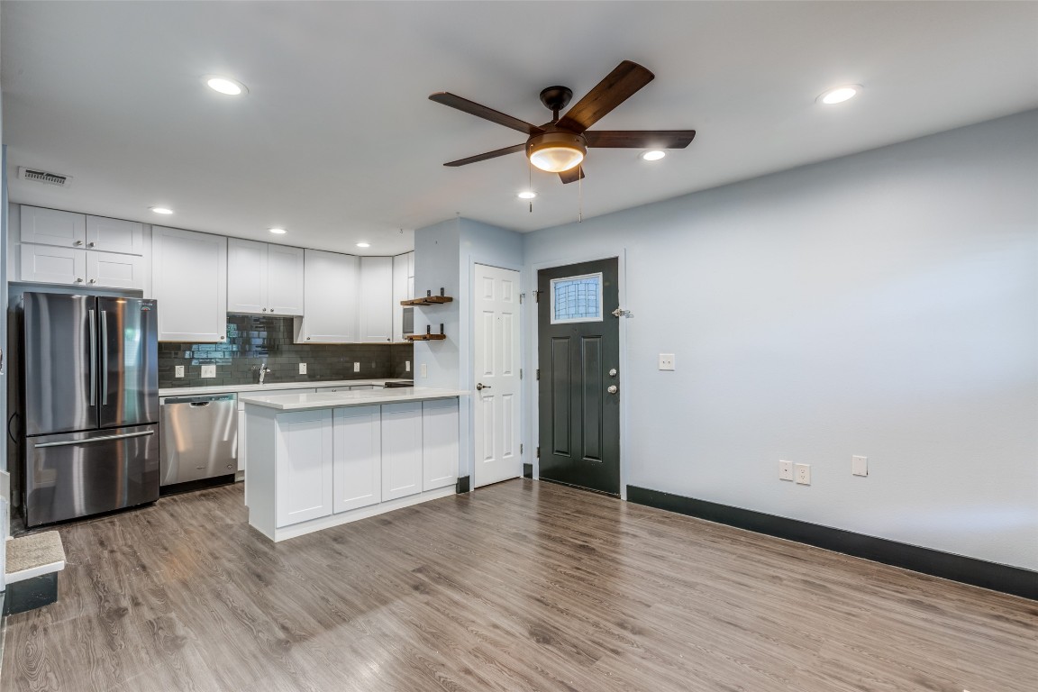 935 La Posada Drive, Unit 155 Austin, TX 78752 - Photo 5 of 25 Kitchen featuring appliances with stainless steel finishes, a peninsula, light wood-style flooring, backsplash, and white cabinets
