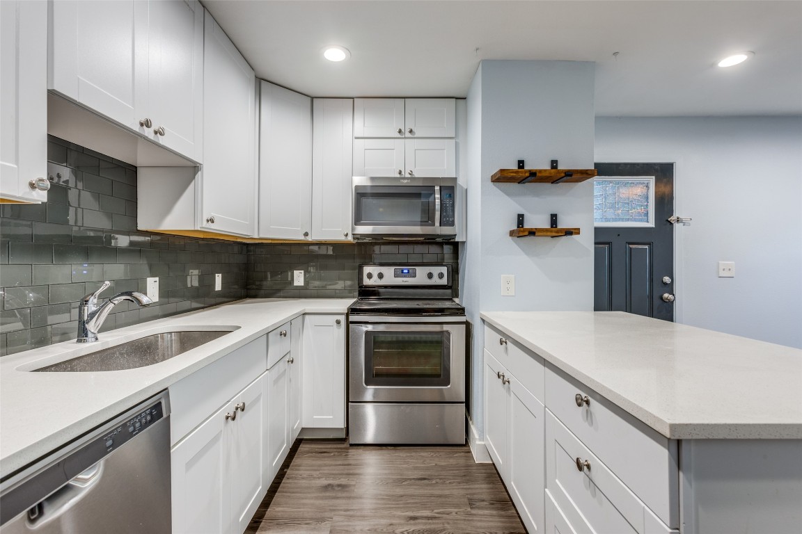 935 La Posada Drive, Unit 155 Austin, TX 78752 - Photo 9 of 25 Kitchen with stainless steel appliances, decorative backsplash, white cabinets, light stone counters, and recessed lighting