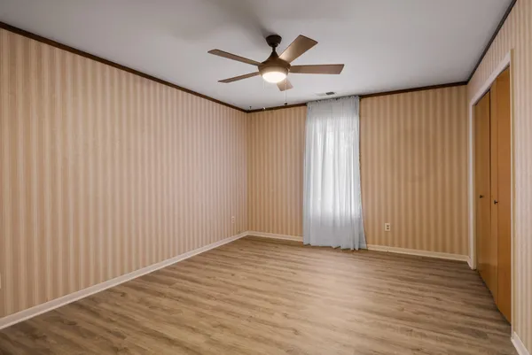 an empty room with wooden floor chandelier fan and windows