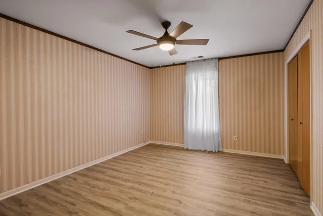 an empty room with wooden floor chandelier fan and windows