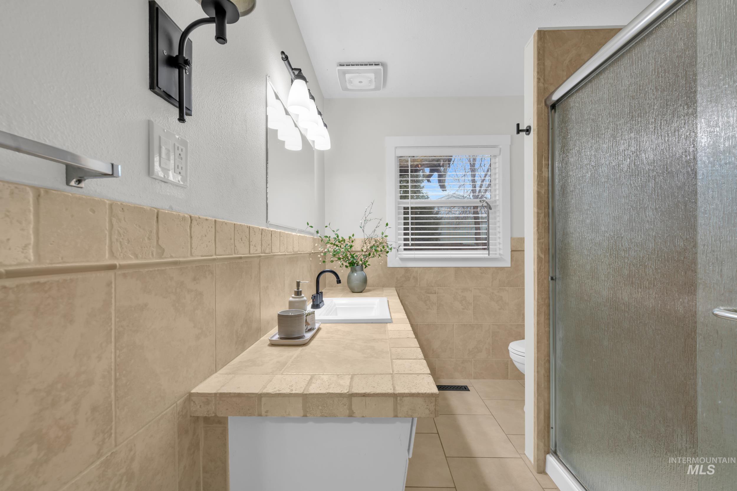 2908 Meadowbrook Drive Boise, ID 83705 - Photo 17 of 29 Full bath with vanity, a shower stall, tile walls, light tile patterned flooring, and a wainscoted wall