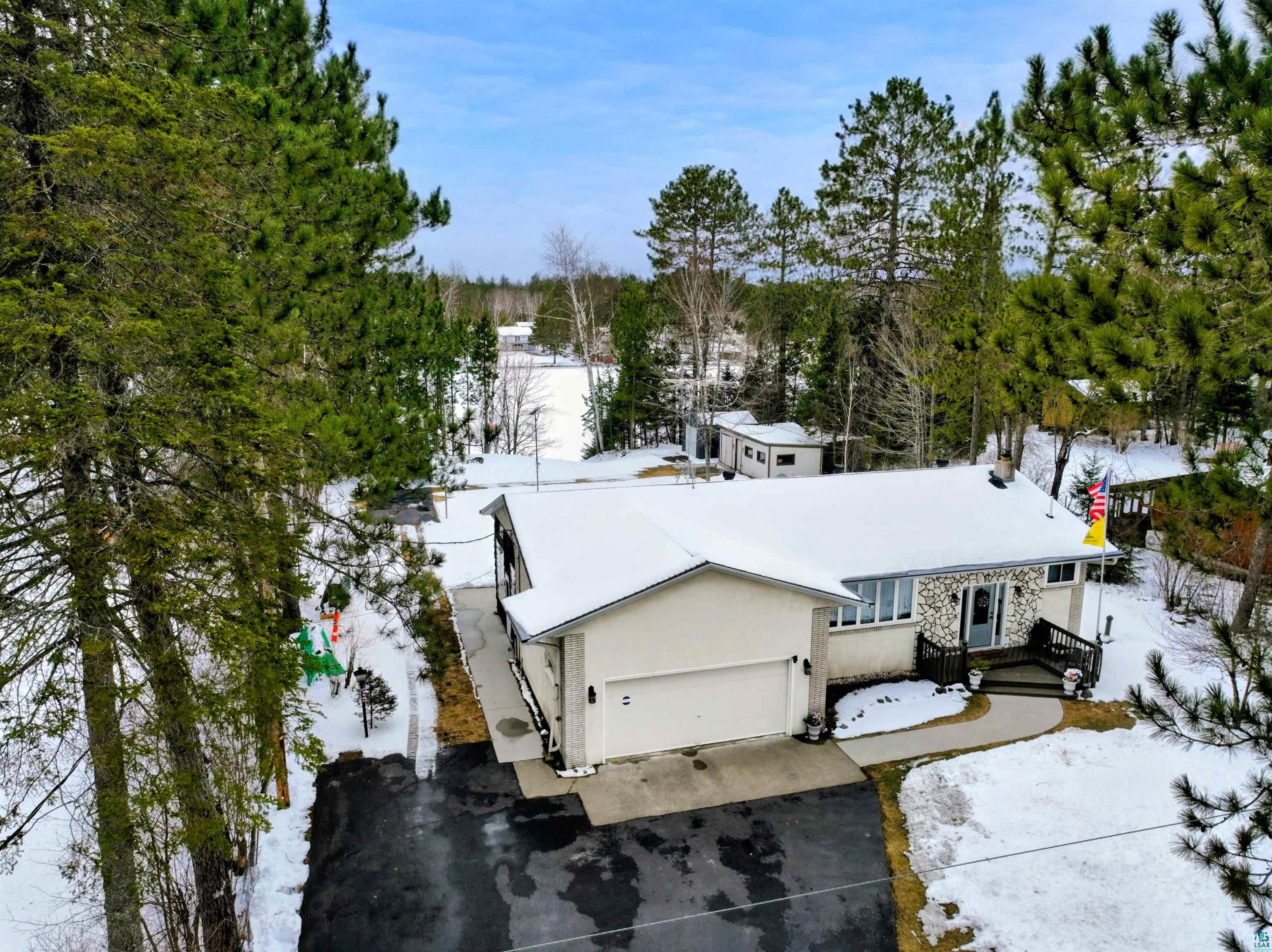View of front of property featuring an attached garage, driveway, stucco siding, and view of wooded area