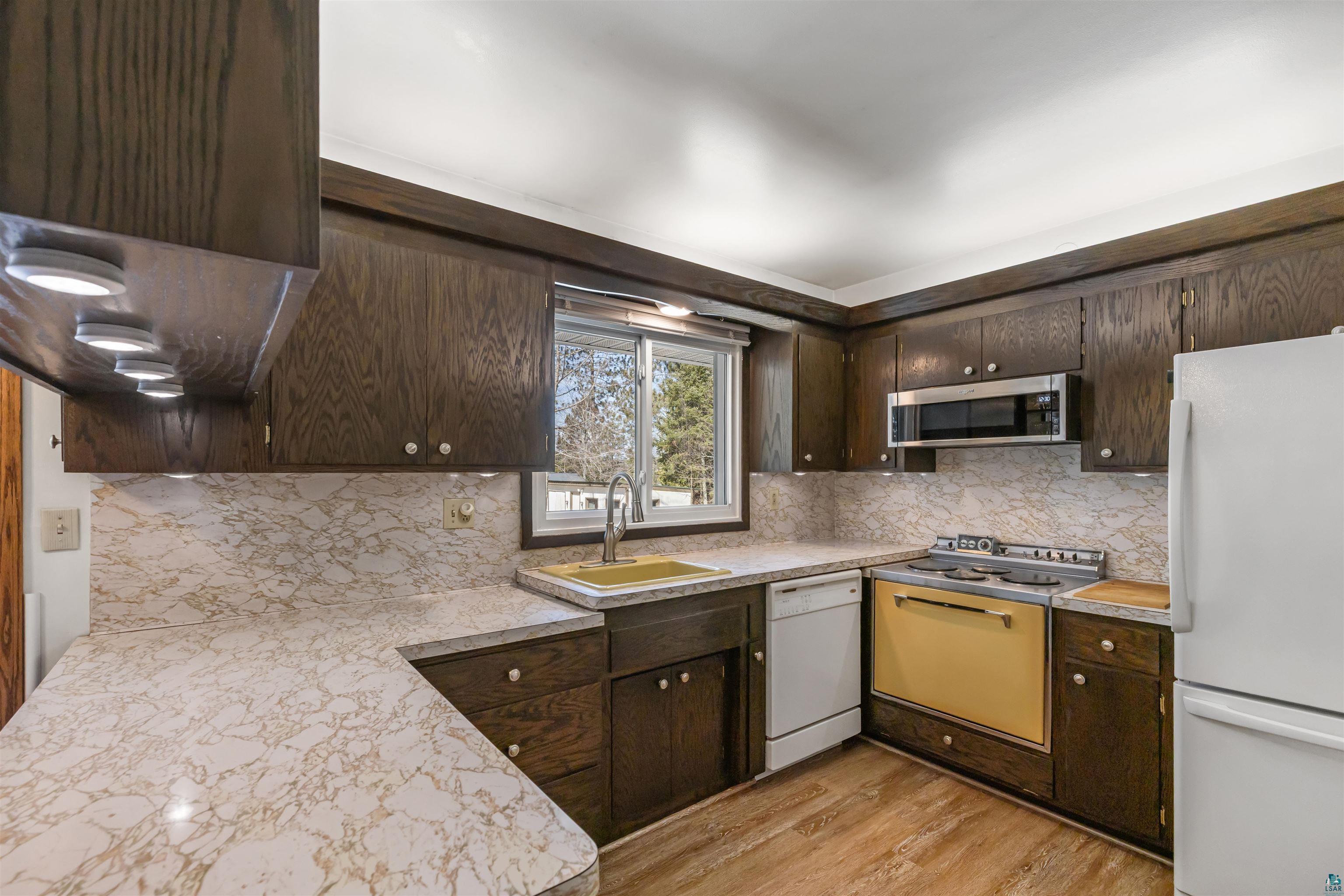 3975 Long Lake Shores Road Eveleth, MN 55734 - Photo 15 of 79 Kitchen with dark wood finish cabinetry, white appliances, light countertops, light wood finished floors, and decorative backsplash
