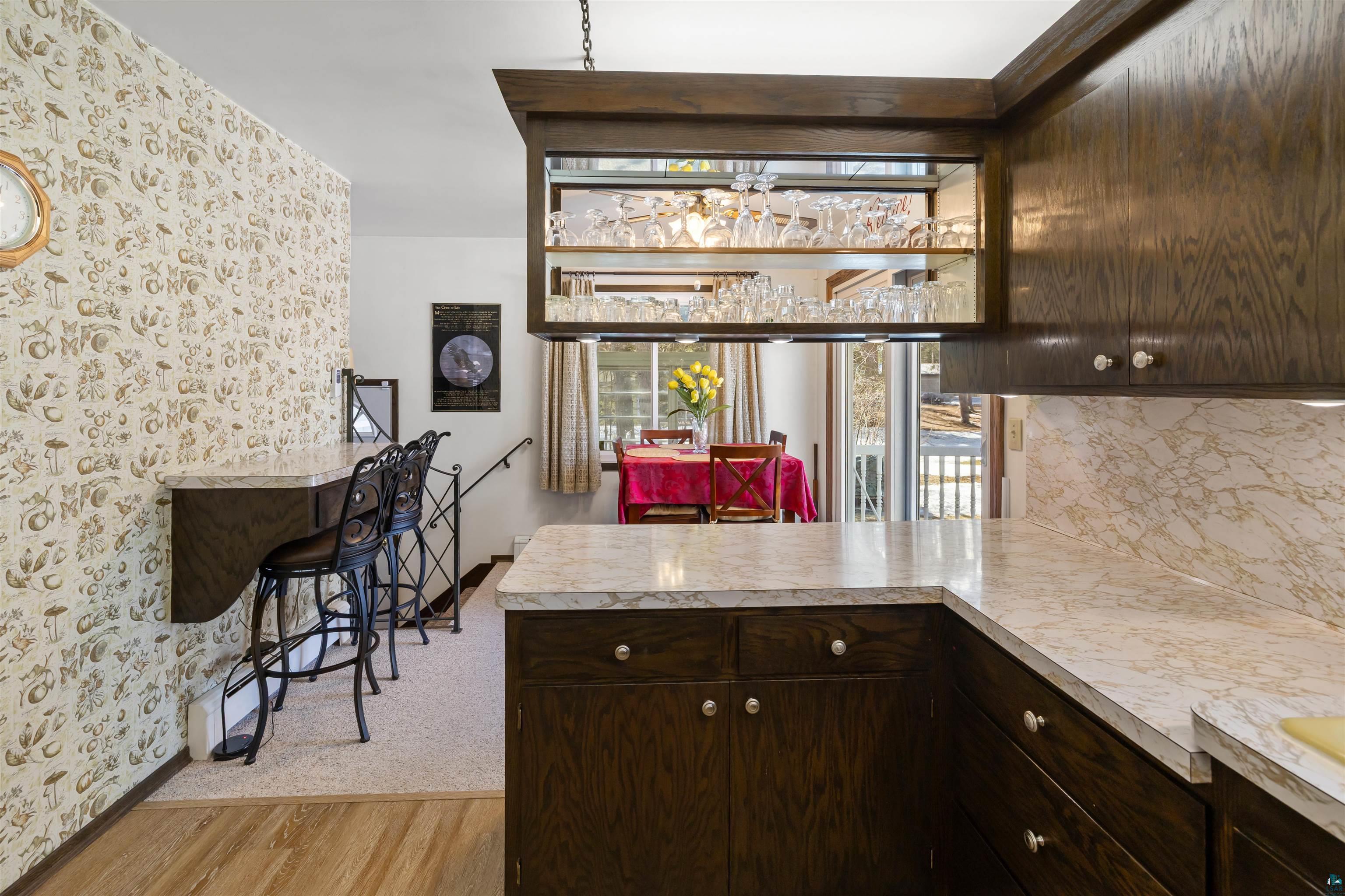 3975 Long Lake Shores Road Eveleth, MN 55734 - Photo 22 of 79 Kitchen with dark wood finish cabinets, a peninsula, wallpapered walls, light wood finished floors, and tasteful backsplash