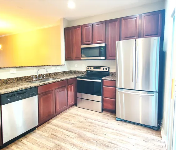 a kitchen with stainless steel appliances granite countertop a refrigerator stove a sink and a granite counter tops with wooden floors