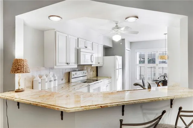 a kitchen with stainless steel appliances granite countertop a sink a refrigerator and white cabinets with wooden floor