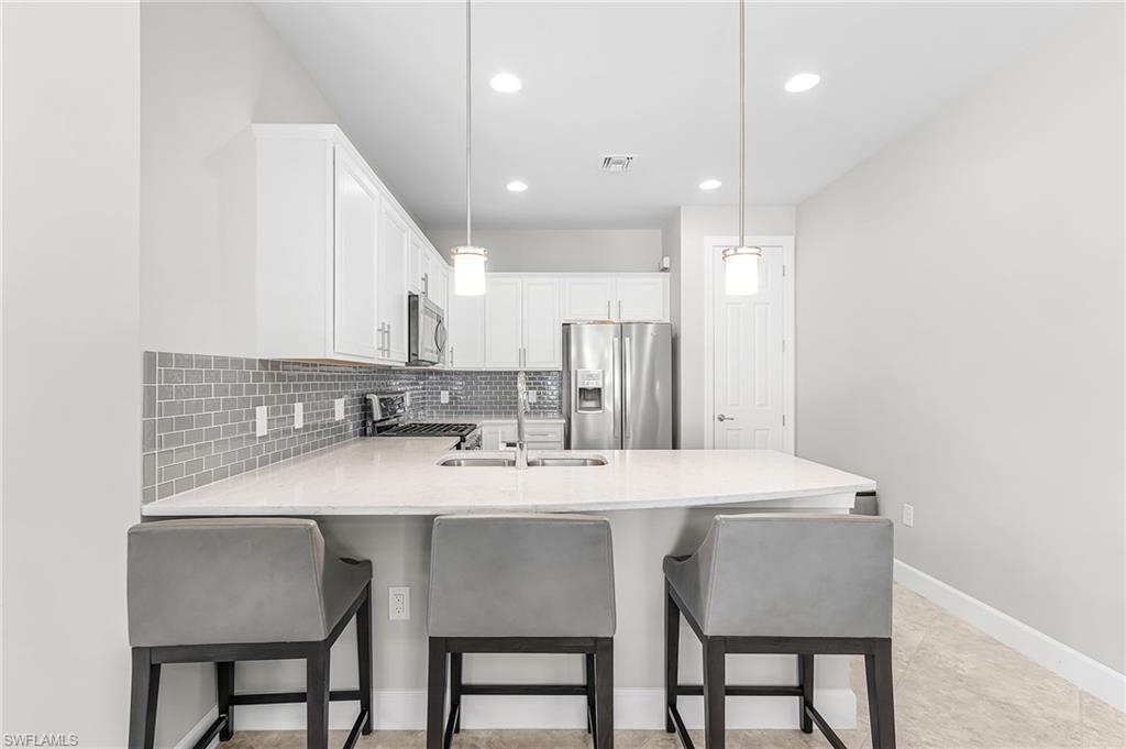 20131 Torch Key Way Estero, FL 33928 - Photo 9 of 47 Kitchen with a peninsula, white cabinets, stainless steel appliances, light stone countertops, and decorative backsplash