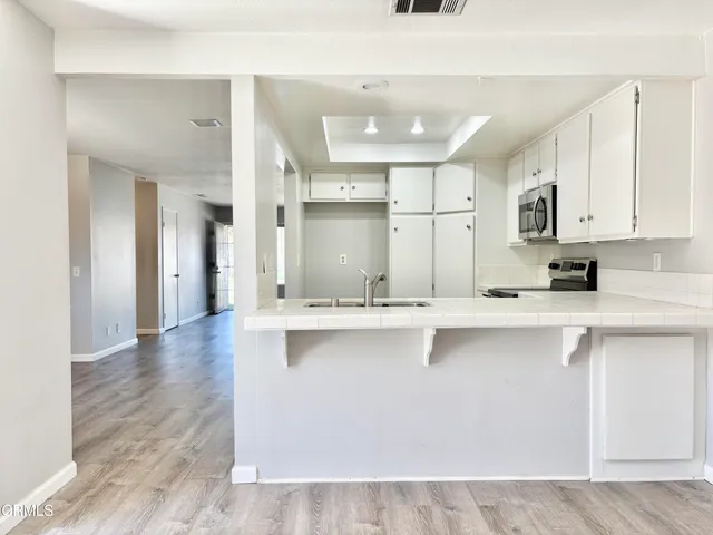 a large kitchen with stainless steel appliances a large counter top a stove a refrigerator with white cabinets and wooden floor