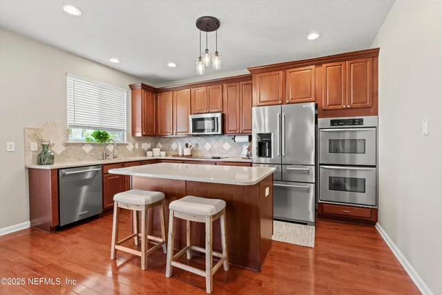 a kitchen with stainless steel appliances granite countertop a refrigerator a stove a sink a dining table and chairs with wooden floor