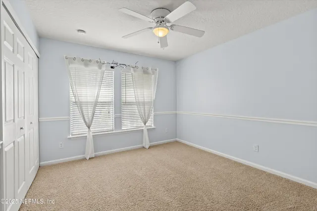 an empty room with chandelier fan and windows