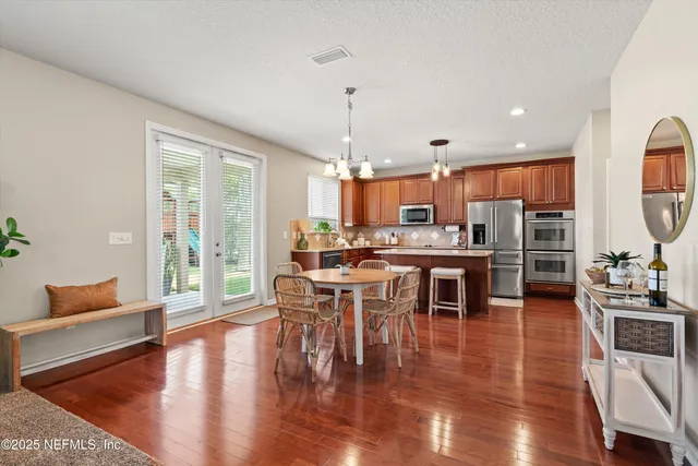 a kitchen with stainless steel appliances granite countertop a stove top oven a sink a dining table and chairs with wooden floor