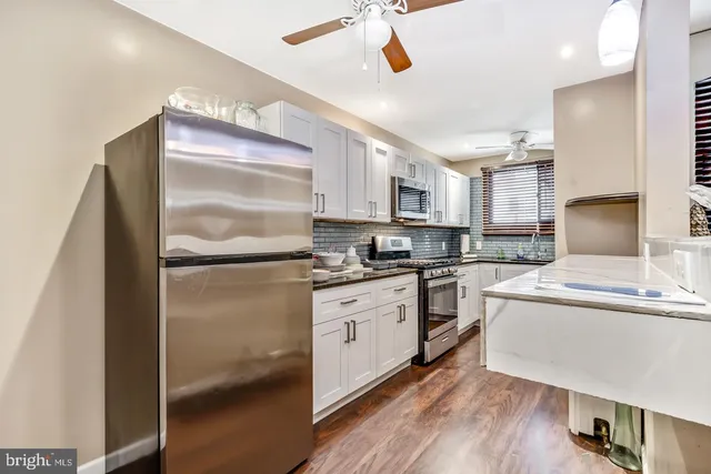 a kitchen with stainless steel appliances granite countertop a refrigerator a sink dishwasher a stove and white countertops with wooden floor