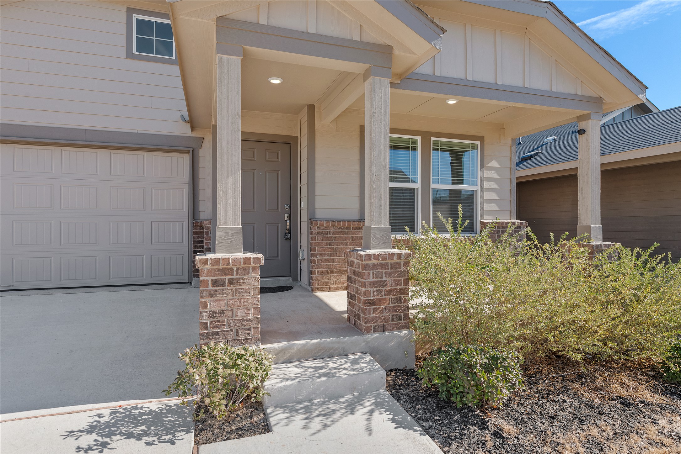 Welcome to 153 Sormonne Loop. 
Property entrance featuring covered porch, board and batten siding, driveway, an attached garage, and brick siding