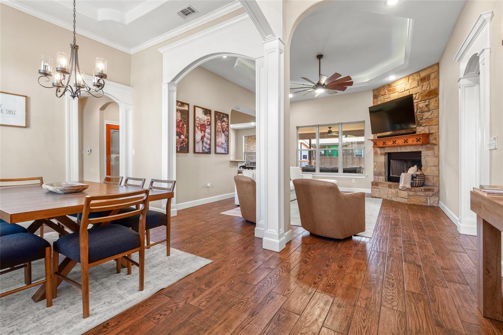 Wood-finish flooring throughout, tray ceiling, stone-clad fireplace, and arched doorways