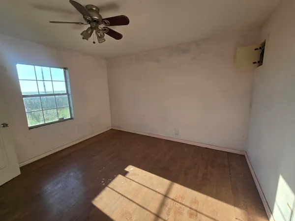 an empty room with wooden floor fan and windows