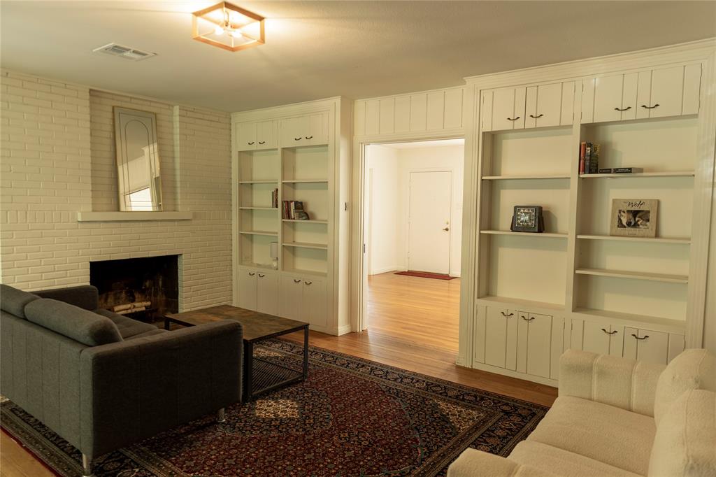 3228 Colcord Avenue Waco, TX 76707 - Photo 4 of 29 Living room featuring a brick fireplace with a mantel, extensive built-in shelving, wood-finish flooring, and a flush mount ceiling light fixture