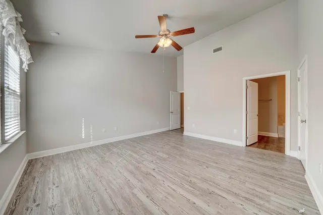 an empty room with wooden floor chandelier fan and windows