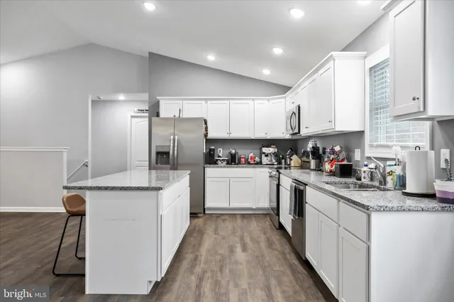 a kitchen with stainless steel appliances granite countertop a stove top oven a sink a refrigerator and white cabinets with wooden floor