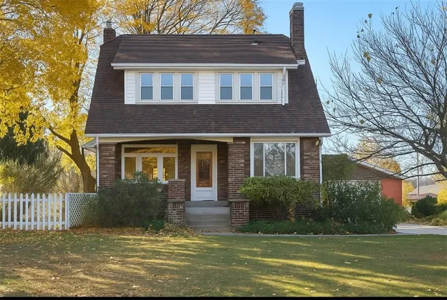a view of a brick house with a yard plants and large tree